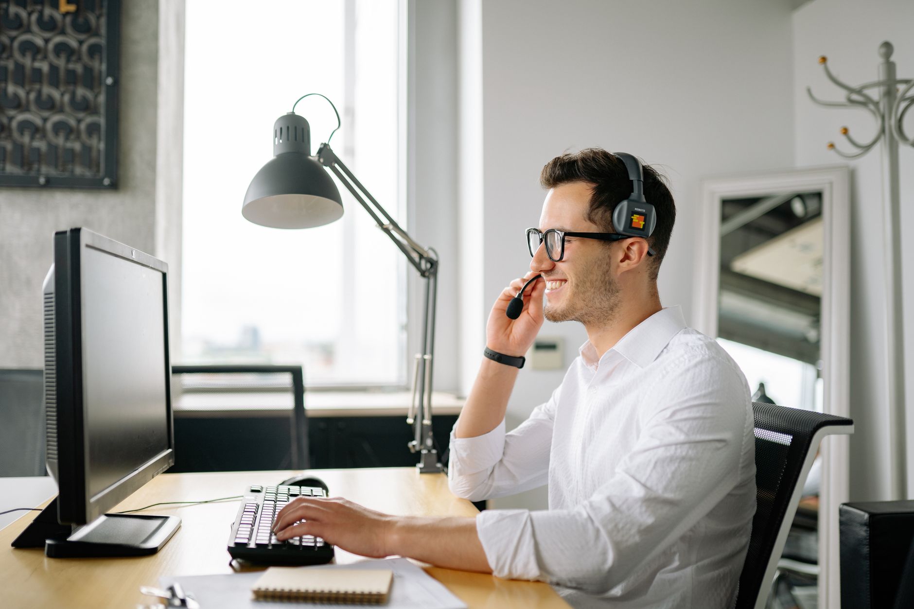 Smiling man wearing headset working at computer in bright office — illustrating: VoIP vs Traditional Phone Lines: Which Costs Less for Your Central Florida SMB?